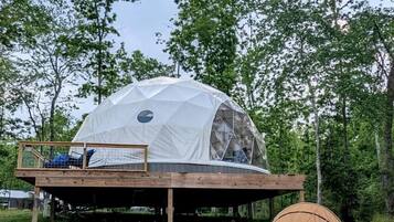 A geodesic dome structure with a wooden deck, seating area, and a small table.