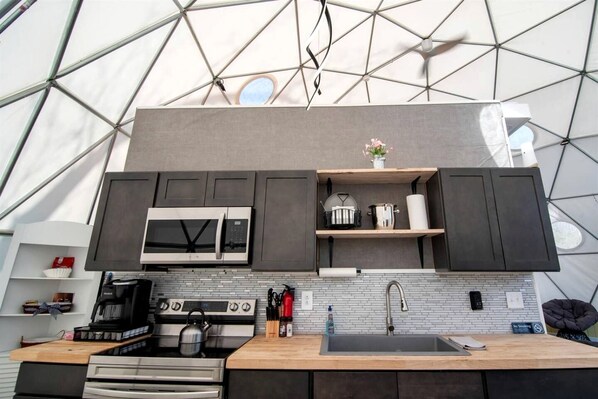 A modern kitchen with a microwave, stove, and sink, under a geodesic dome structure.