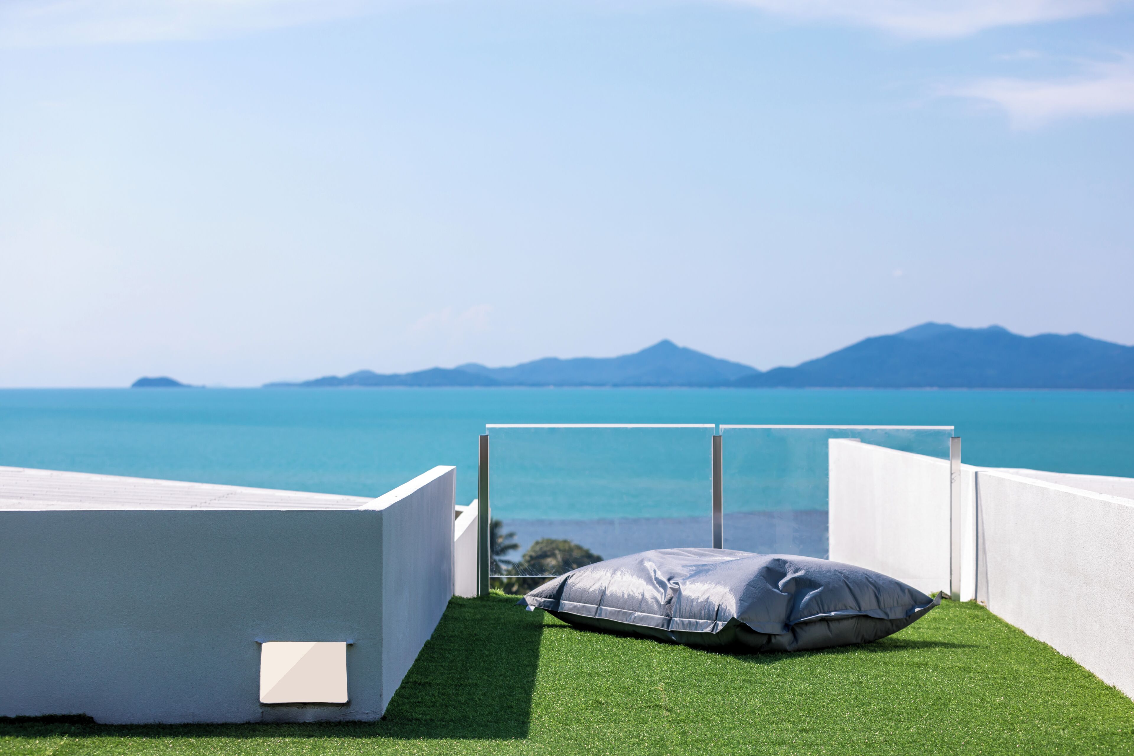 Un balcon avec un revêtement de sol en gazon synthétique, un mur blanc et une vue sur la mer et les montagnes.