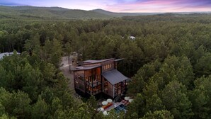 Une cabane moderne entourée d’une forêt dense, dotée d’une terrasse et d’un espace salon extérieur.