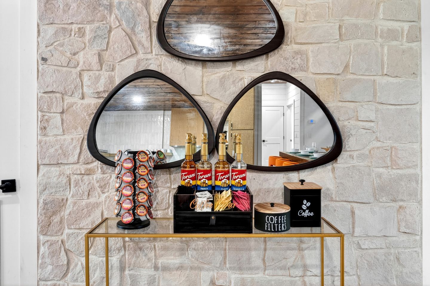A stone wall with two heart-shaped mirrors, a coffee station with Torani and coffee filters, and a wooden box labeled 'Coffee Filters'.