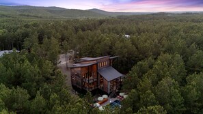 A modern cabin surrounded by dense forest, with a deck and outdoor seating area. - Luxury Cabin with Heated Pool, Sauna & Hot Tub Retreat in Broken Bow, Oklahoma (Broken Bow)