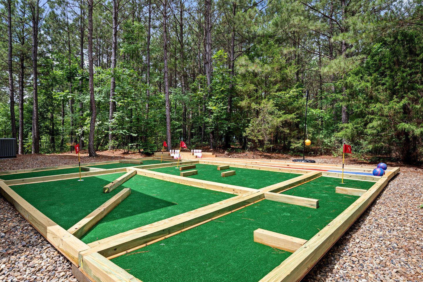 A miniature golf course with wooden structures and green artificial turf, surrounded by a forest.