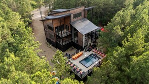 A modern two-story house with a deck and a pool, surrounded by dense forest. - Luxury Cabin with Heated Pool, Sauna & Hot Tub Retreat in Broken Bow, Oklahoma (Broken Bow)