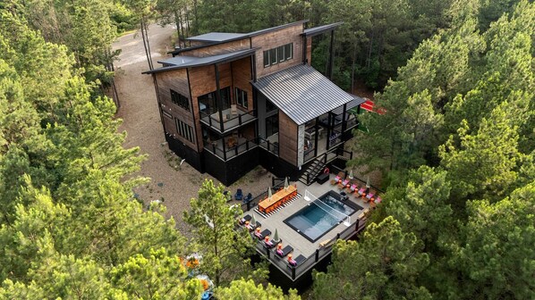 Ein modernes, zweistöckiges Haus mit Terrasse und Pool, umgeben von dichtem Wald.