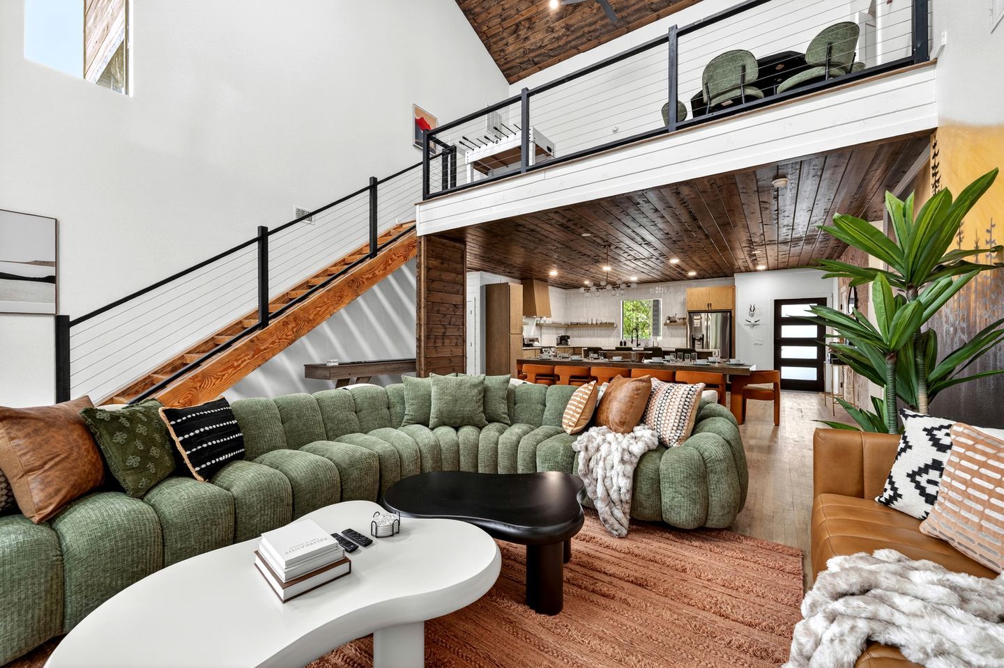 A spacious living area with a green sectional sofa, a white coffee table, and a kitchen in the background.