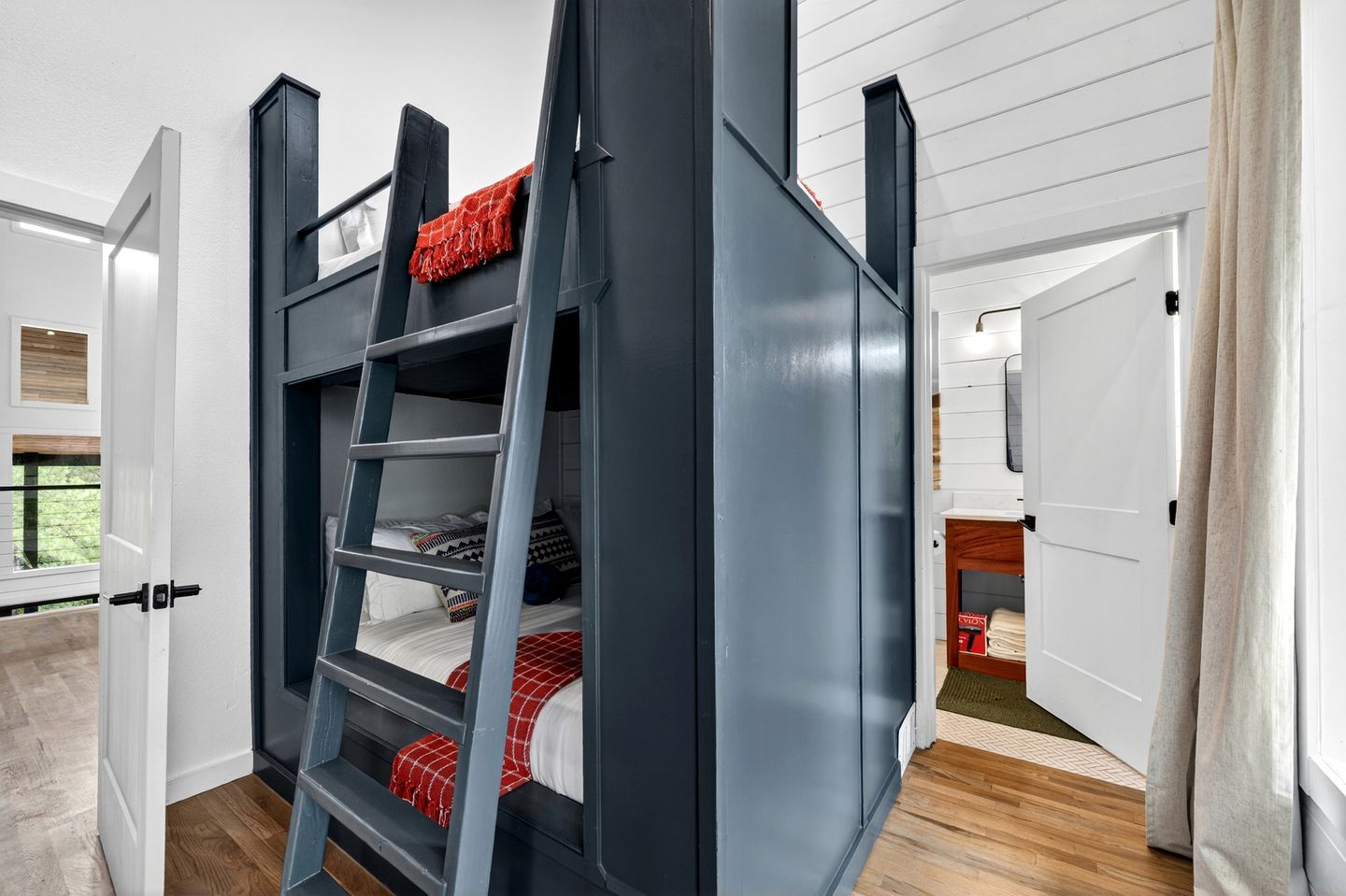 A bunk bed with a ladder, white walls, and a wooden floor.