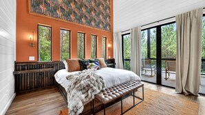 Une chambre avec un grand lit, un banc, une vue sur l’extérieur et un tableau accroché au mur.