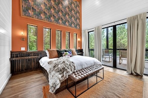 A bedroom with a large bed, a bench, a view of the outdoors, and a painting on the wall. - Luxury Cabin with Heated Pool, Sauna & Hot Tub Retreat in Broken Bow, Oklahoma (Broken Bow)