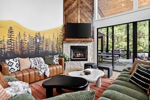 A modern living room with a fireplace, leather sofa, and a mural of trees. - Luxury Cabin with Heated Pool, Sauna & Hot Tub Retreat in Broken Bow, Oklahoma (Broken Bow)