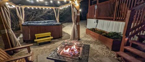 Une terrasse extérieure dotée d’un foyer, de sièges en bois, d’un jacuzzi et de guirlandes lumineuses.