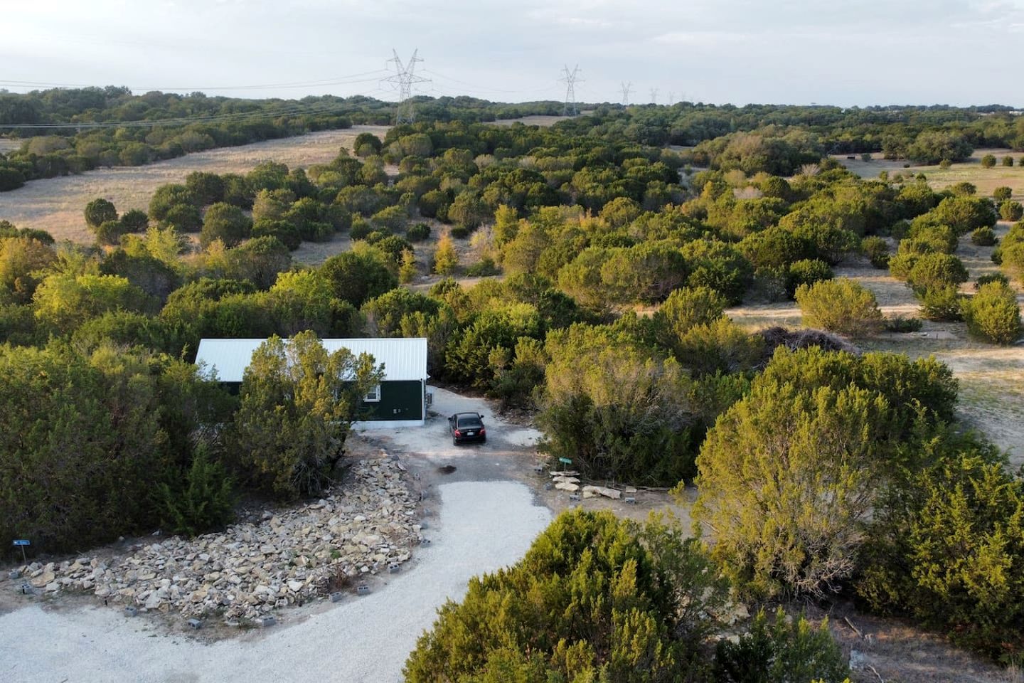 Propiedad rural con una construcción pequeña, un camino de grava y vegetación circundante.