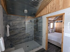 En bruser med glasdøre, et træloft og en seng med hvid madras og puder.
