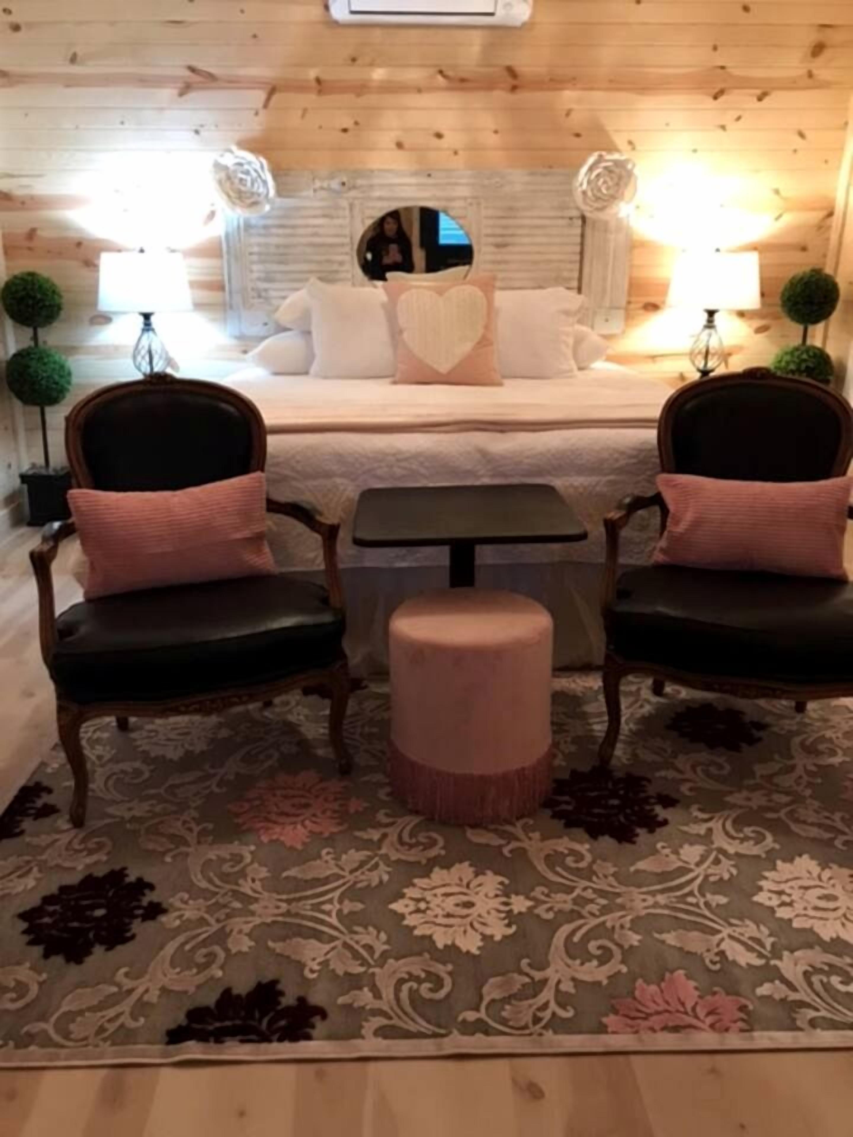 A cozy room with a bed, two chairs, a small table, and a round ottoman.