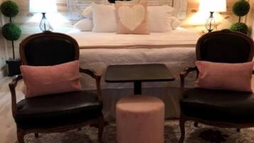 A cozy room with a bed, two chairs, a small table, and a round ottoman.