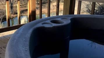 Een hottub op een houten terras met uitzicht op bomen en een waterlichaam.