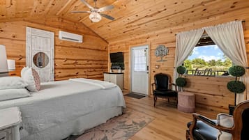 Een slaapkamer in een blokhut met een bed, een stoel, een bureau en een raam met gordijnen.