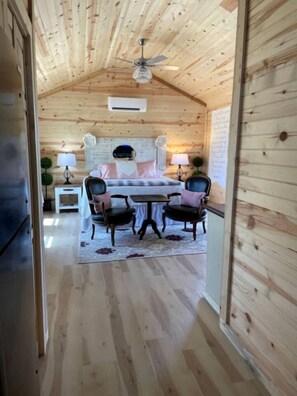 A wooden interior with a bed, two chairs, a table, a ceiling fan, and a small side table with a lamp. - Lovely Cabin Rental in Fredericksburg with a Hot Tub (Fredericksburg)