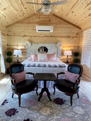 A cozy wooden room with a bed, two chairs, a small table, and a ceiling fan. - Lovely Cabin Rental in Fredericksburg with a Hot Tub (Fredericksburg)