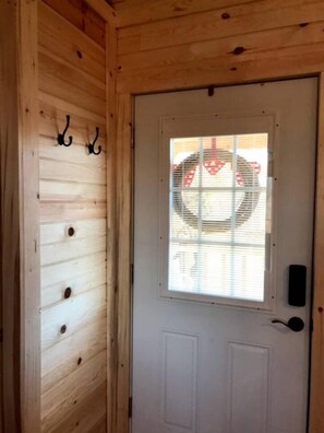A wooden door with a window, a doorbell, and a wall-mounted hook. - Lovely Cabin Rental in Fredericksburg with a Hot Tub (Fredericksburg)