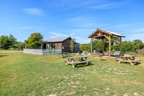 En rustik utomhusmiljö med en timmerstuga, picknickbord och en överbyggd sittplats.