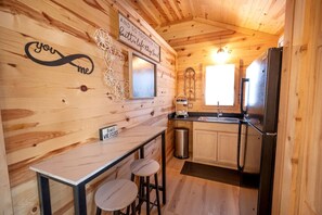 Interno di una baita in legno con angolo cottura, sgabelli da bar, un orologio a vino e decorazioni murali.