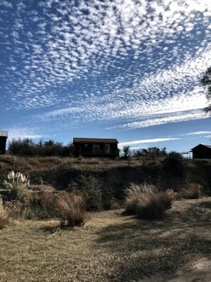 A remote cabin with a dirt path leading to it, surrounded by dry grass and shrubs. - Lovely Cabin Rental in Fredericksburg with a Hot Tub (Fredericksburg)