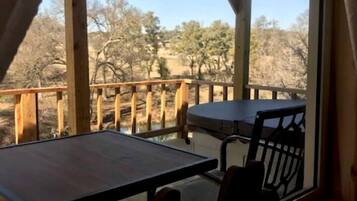 A wooden deck with a table and chairs, a view of trees, and a clear sky.