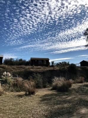 A remote cabin with a dirt path leading to it, surrounded by dry grass and shrubs. - Lovely Cabin Rental in Fredericksburg with a Hot Tub (Fredericksburg)