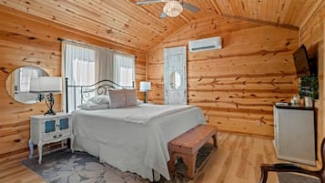 A wooden cabin bedroom with a bed, bedside tables, a bench, a mirror, an air conditioning unit, and a ceiling fan.