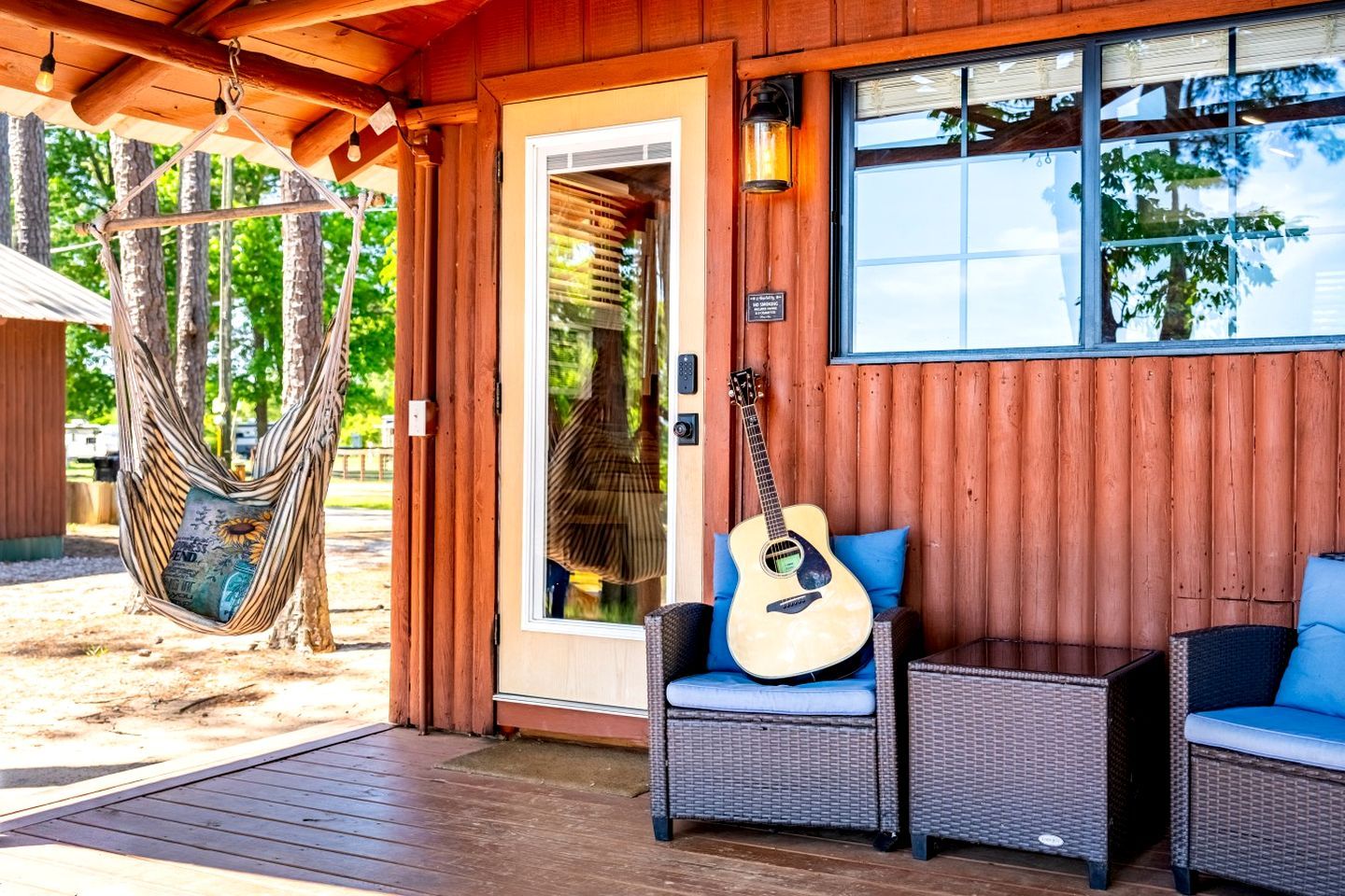 En byggnad med träfasad, en hängmatta, en gitarr, flätade stolar och en dörr.