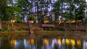 A lakeside property with a dock, a wooden staircase, and several illuminated cabins. - Beautiful Cabin by the Lake Nestled in Sabine National Forest for a Romantic Retreat in Hemphill, Texas (Hemphill)