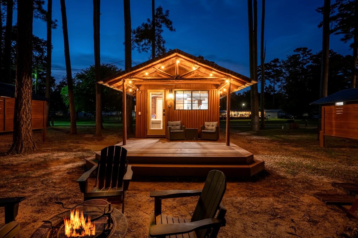 A wooden cabin with a porch, a fire pit, and two chairs.