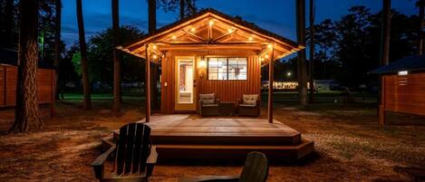 A wooden cabin with a porch, a fire pit, and two chairs.