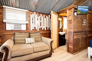 A wooden cabin interior with a sofa, wooden wall decor, a television, and a bathroom.