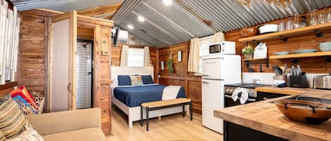 Una habitación compacta tipo cabaña con cama, kitchenette y un pequeño rincón de descanso.