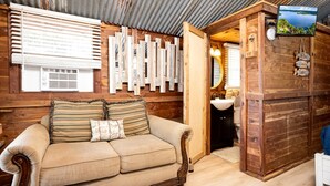 A wooden cabin interior with a sofa, wooden wall decor, a television, and a bathroom. - Beautiful Cabin by the Lake Nestled in Sabine National Forest for a Romantic Retreat in Hemphill, Texas (Hemphill)