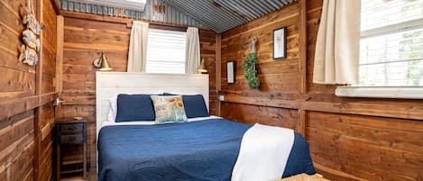 Un dormitorio de cabaña de madera con cama, banco y ventana con cortinas.
