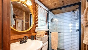A wooden cabin bathroom with a sink, mirror, towel rack, and shower. - Beautiful Cabin by the Lake Nestled in Sabine National Forest for a Romantic Retreat in Hemphill, Texas (Hemphill)
