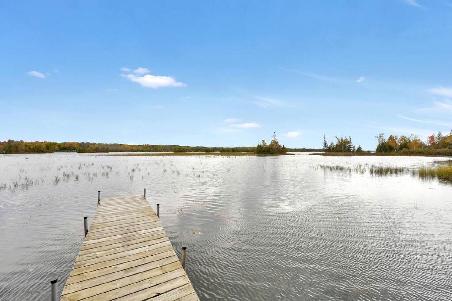 Une jetée en bois s’étendant sur une étendue d’eau calme, sous un ciel dégagé.