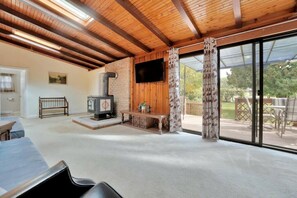 A spacious living area with a fireplace, a television, and a sliding glass door leading to an outdoor deck. - Rustic Family Cottage with Spectacular Sunset Views on Canal Lake, Near Kawartha Lakes, Ontario (Kirkfield)