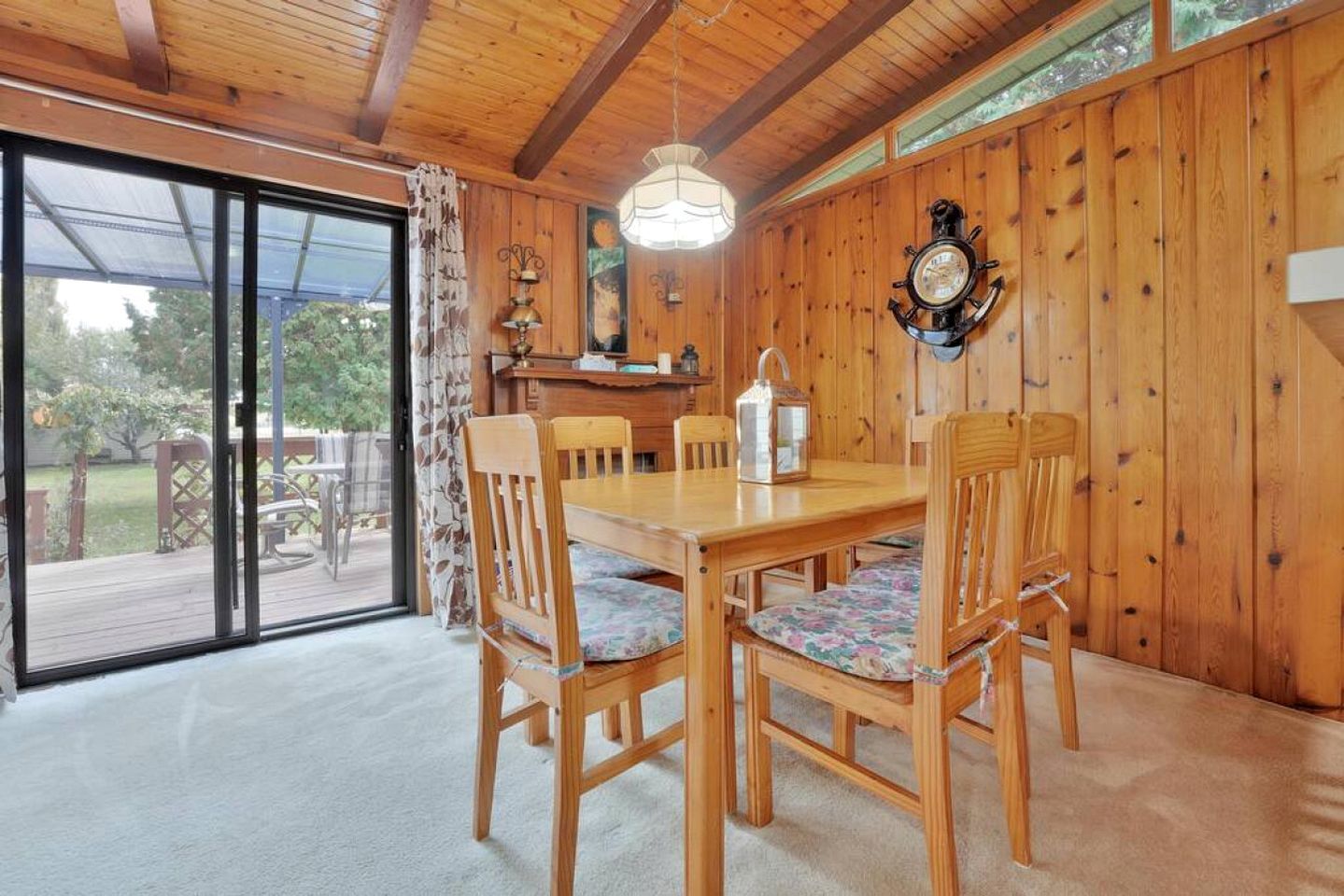 A wooden dining room with a table and chairs, a clock on the wall, and a view through a glass door to the outside.
