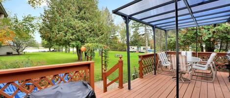 A wooden deck with a covered patio area, outdoor furniture, and a lawn.