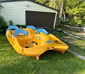 En gul uppblåsbar båt med blå säten, parkerad på gräset bredvid en byggnad.