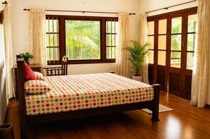 A bedroom with a bed, a window, a potted plant, and a wooden door. - Enteveedu Homestay (Panamaram)