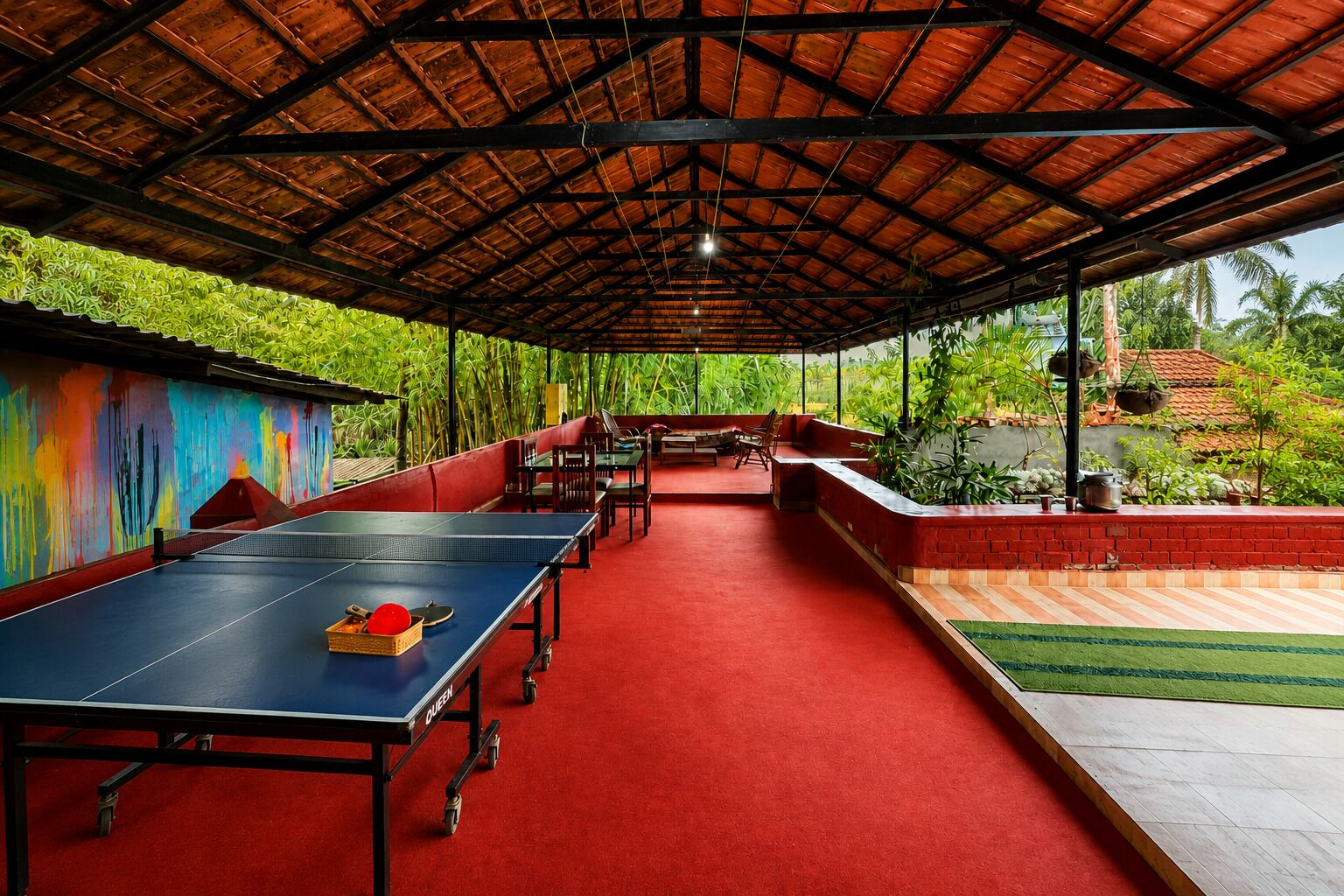 An indoor badminton court with a red carpet, seating area, and a view of greenery outside.