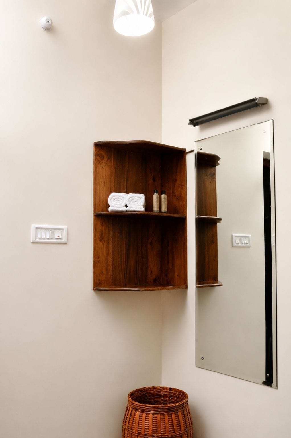 A corner of a room with a wooden shelf holding towels and toiletries, a mirror, and a wicker basket.