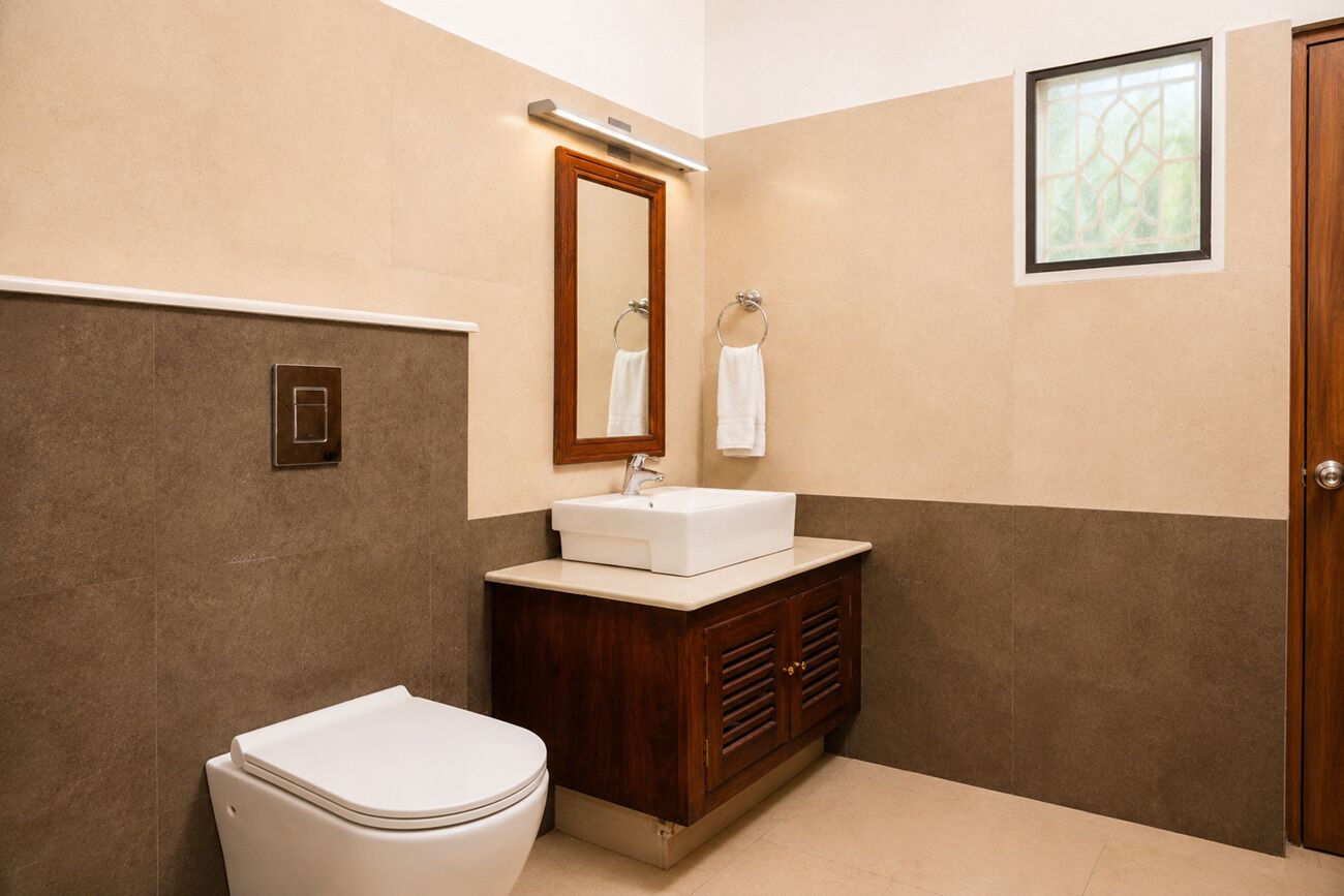 A bathroom with a toilet, sink, vanity, mirror, and a window.