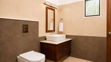 A bathroom with a toilet, sink, vanity, mirror, and a window.