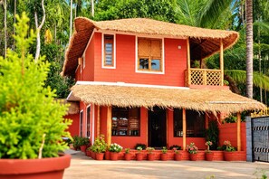 A two-story building with a thatched roof, surrounded by lush greenery and potted plants. - Enteveedu Homestay (Panamaram)